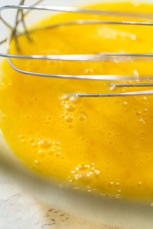 A close-up view of a yellow mixture being whisked in a glass mixing bowl, showing the texture and...