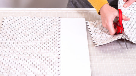 In the process of mounting peel and stick mosaic tiles onto a foam board, perfect for enhancing a...