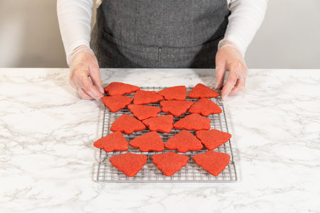 A cooling rack filled with red, tree-shaped gingerbread cookies, freshly baked and arranged in rows. These Red Gingerbread Cookies are cooling on the counter, showcasing their vibrant color and festive shapes.の写真素材
