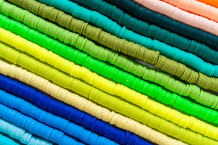A vibrant collection of clay beads, neatly arranged by color on a white table, ready to inspire...