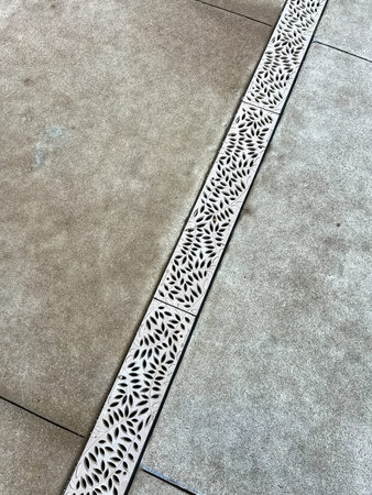 A close-up view of a decorative drain cover embedded in a concrete surface The patterned design adds...