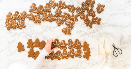 A festive arrangement of decorated gingerbread man cookies spread across a marble countertop, surrounded by holiday-themed baking tools, creating a cheerful and seasonal vibe.の写真素材