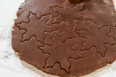 A close-up of snowflake-shaped cookie cutters pressed into Chocolate Ginger Sugar Cookie dough,...