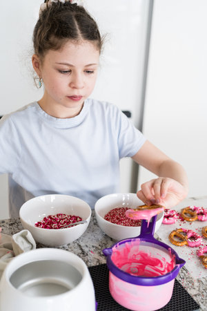 With focused attention, this budding culinary artist dips pretzels into a pot of melted chocolate, creating sweet delights in the warmth of a well-lit home kitchen.の写真素材