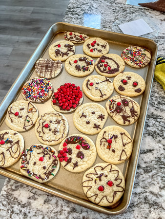 A baking sheet filled with freshly baked sugar cookies decorated with chocolate drizzle, sprinkles,...