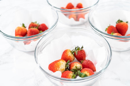 Bright red strawberries rest in a glass bowl lined with a paper towel on a white napkin.の写真素材
