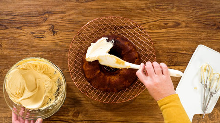 Flat lay. A gingerbread bundt cake being generously frosted with salted caramel frosting and topped...