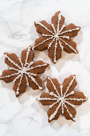 Top-down view of three chocolate ginger snowflake cookies, each beautifully decorated with royal...