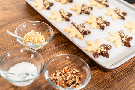 Creating cutout sugar cookies, partially dipped in chocolate and topped with hazelnut pieces, placed...