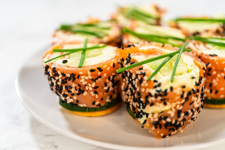 A beautiful arrangement of smoked salmon jumbo cream cheese rolls served on a plate. The rolls are evenly garnished with fresh chives and feature a crunchy sesame seed coating. This dish is a perfect centerpiece for festive parties and elegant gatherings.の写真素材