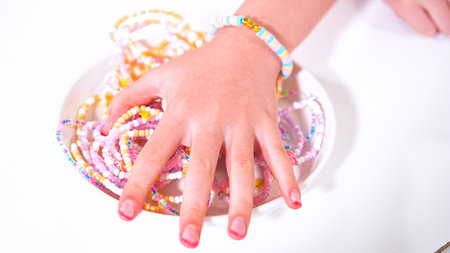 Delicate fingers of a young girl navigate through a treasure trove of bright, multicolored beads, each compartment revealing a new hue to choose from. Shes immersed in the joyful task of stringing together a handmade bracelet, with golden beads and pearls lying nearby to add a touch of sparkle to her creation.の写真素材
