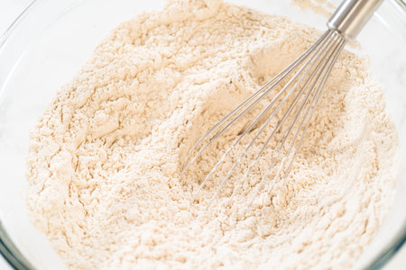 Close-up view of flour being whisked in a glass bowl, part of the initial steps in preparing Classic Gingerbread Cookie Dough. The whisk helps to evenly mix the dry ingredients before combining with wet ingredients.の写真素材