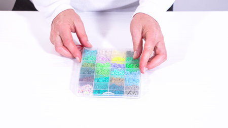 Womans hands gracefully poised over a collection of beads, sorted by color in transparent...