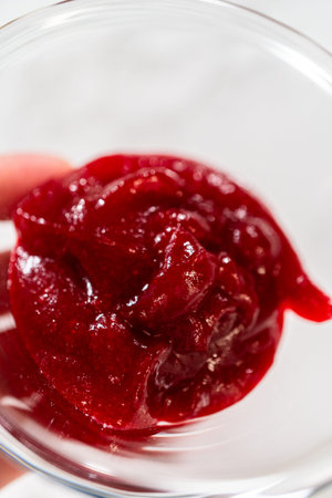 A close-up of vibrant, homemade cranberry sauce in a clear glass dish. The rich red sauce appears...
