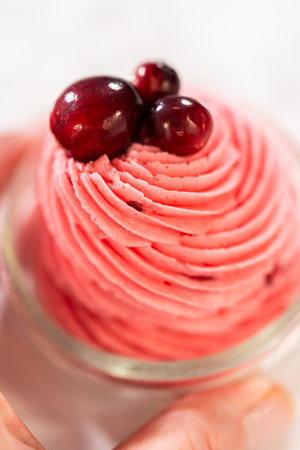 A swirl of vibrant cranberry buttercream piped into a glass jar and topped with fresh cranberries. This creamy, tart frosting is perfect for cookies, cakes, and holiday desserts.の写真素材