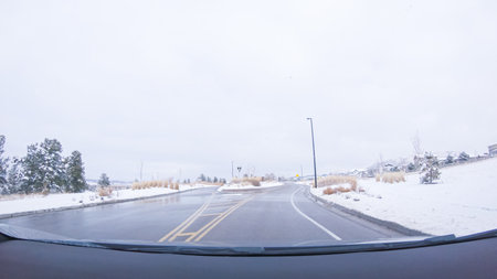 The early morning brings a quiet drive through a newly built suburban neighborhood, with fresh snow blanketing the road and houses under a still-dark sky.の写真素材