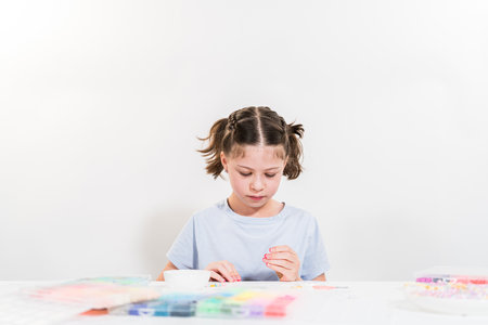 Little girl enjoys crafting colorful bracelets with vibrant clay beads set.の写真素材