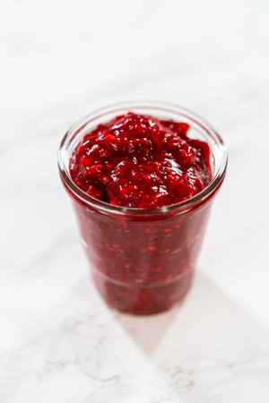 Freshly made Raspberry Cake Filling is carefully poured into a glass jar - ready to be used to add a...