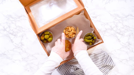 Flat lay. Hands are meticulously adding fresh olives and pickles to a bowl, complementing a...