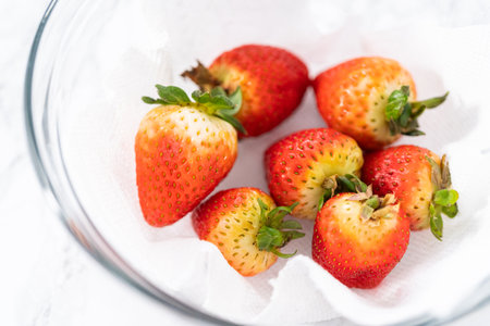 Freshly washed and dried strawberries are carefully arranged in a glass bowl lined with paper towel, ready for snacking or further use.の写真素材