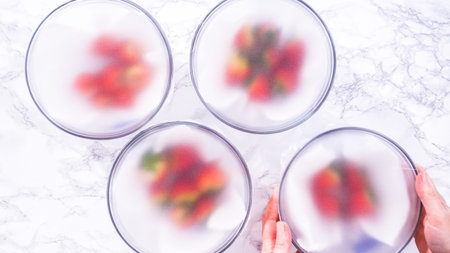 Flat lay. Strawberries, freshly washed and dried, are neatly stored in a glass bowl lined with a paper towel and securely covered with plastic wrap to maintain freshness.の写真素材