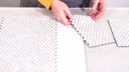 In the process of mounting peel and stick mosaic tiles onto a foam board, perfect for enhancing a...