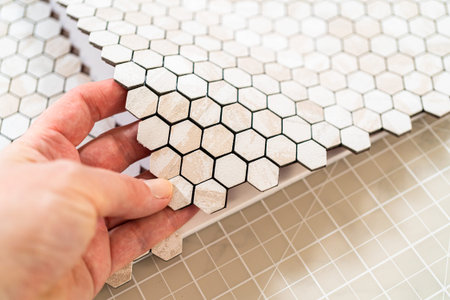In the process of mounting peel and stick mosaic tiles onto a foam board, perfect for enhancing a...