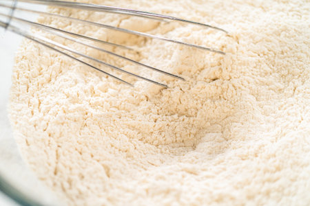 A whisk blends flour in a glass bowl during the early stages of cookie dough preparation. Ideal for baking guides, how-to content, and recipe posts. This image is part of the recipe for Classic Sugar Cookie Dough for Cutout Cookies. This image is part of the Easter Cookie Sandwich with Raspberry Buttercream recipe.の写真素材