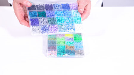 Woman hands gracefully poised over a collection of beads, sorted by color in transparent organizers....