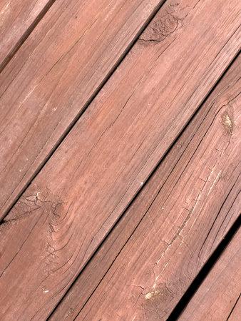 Close-up image of weathered brown wooden decking boards showing natural wood grain, knots, and...