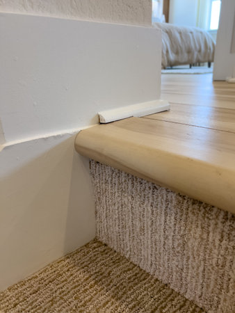 A close-up image of a textured white wall at the top of a staircase, framed with wood and white...