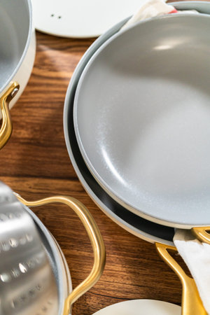 Top-down view of stacked gray nonstick pans with gold handles placed on a wooden countertop. A...