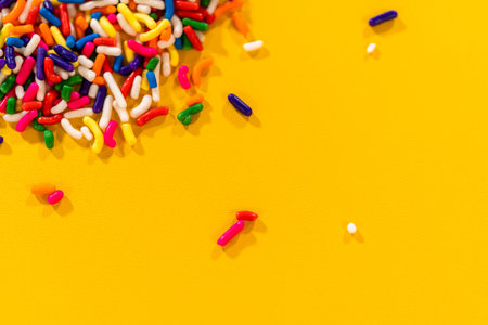 A few candy sprinkles are scattered on a yellow surface in front of a dense pile. The image...