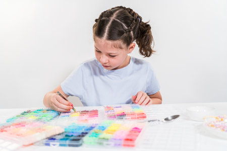 Little girl enjoys crafting colorful bracelets with vibrant clay beads set.の写真素材