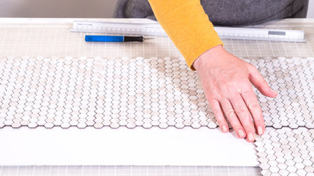 In the process of mounting peel and stick mosaic tiles onto a foam board, perfect for enhancing a...