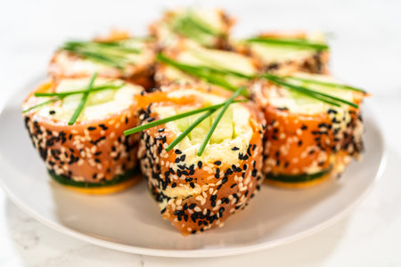 A beautiful arrangement of smoked salmon jumbo cream cheese rolls served on a plate. The rolls are evenly garnished with fresh chives and feature a crunchy sesame seed coating. This dish is a perfect centerpiece for festive parties and elegant gatherings.の写真素材