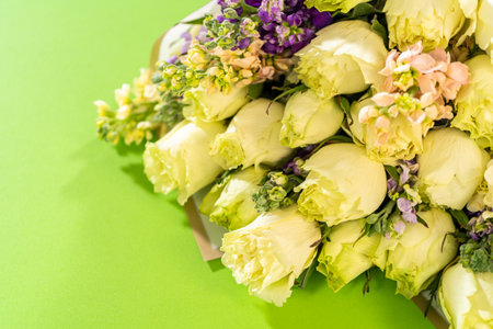 Close-up flat lay of a floral bouquet featuring cream-colored roses mixed with small purple and pink wildflowers. The bouquet is set on a vibrant green background.の写真素材