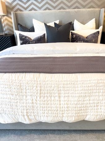 A neatly made bed with white linens and a folded accent throw is placed against a chevron-patterned...