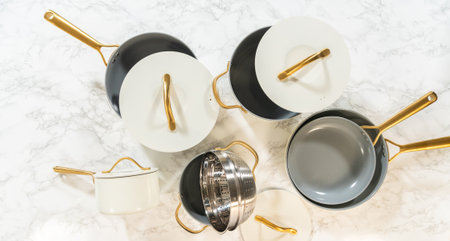 A curated flatlay of ceramic cookware with gold handles, matching lids, and a strainer insert, arranged neatly on a marble kitchen surface. Great for use in kitchen blog posts or catalog designs.の写真素材