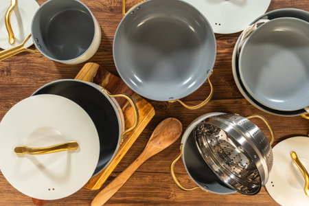 An assortment of cooking pots, pans, and a steamer insert placed alongside wooden utensils and mixing bowls on a wood table.の写真素材