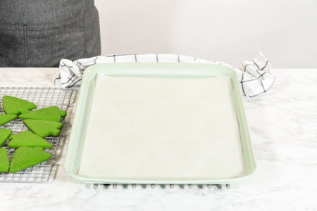 A top-down perspective showing an empty baking tray next to a cooling rack filled with freshly baked...