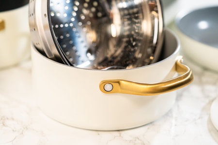 White ceramic pot filled with a shiny stainless steel steamer basket, styled beside matching pots....