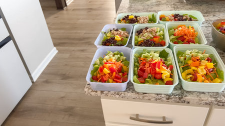 A kitchen scene shows a full meal prep setup with containers of colorful chopped salads on a...
