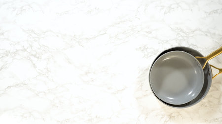 A gray ceramic-coated nonstick frying pan sits on a white marble counter. The scene is minimal with neutral tones and soft natural light.の写真素材