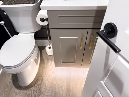 A modern bathroom setup with a white toilet, gray vanity cabinet with gold handles, and a matte black door handle. Soft lighting and wood floors complete the look.の写真素材