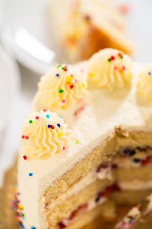 A slice of vanilla cake with fruit and frosting sits on a plate in the foreground. The background shows more cake out of focus, enhancing depth in the image.の写真素材
