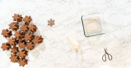 Partially decorated chocolate ginger snowflake cookies displayed on a marble surface, with sugar...