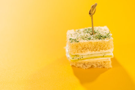 Finger-sized cucumber sandwiches made with soft white bread, herbed cream cheese, and thin cucumber slices. Topped with a sprinkle of fresh dill and secured with bamboo cocktail picks. Ideal for garden parties, bridal showers, or elegant appetizer spreads.の写真素材