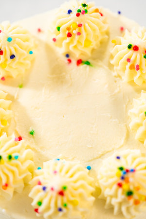 Close-up image showing two prominent swirls of buttercream frosting on the edge of a cake. The frosting is smooth and topped with tiny rainbow sprinkles. The background is softly blurred for depth.の写真素材