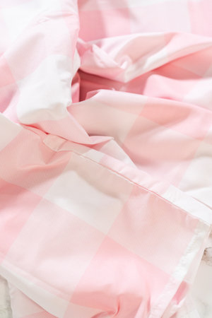 Close macro shot of wrinkled pastel pink and white gingham fabric. Focus on surface texture and cloth detailing with natural shadow lines.の写真素材